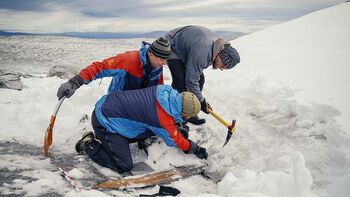 The archaeologists carefully remove the ice above the ski with an ice axe.