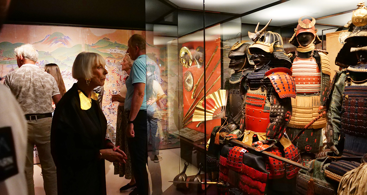 Personer er i et utstillingsrom, en dame ser p? et monter som viser flere samurai-rustninger.