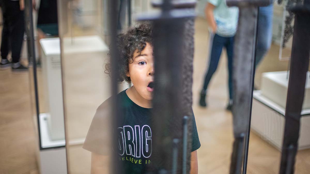 Et barn ser på vikingsverd i en utstilling.