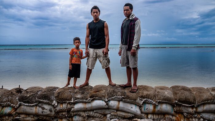 Bilde av to unge menn og en gutt som st?r p? en barrikade foran havet.