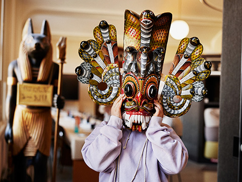 A girl holding a mask with snake ornaments in front of her face.