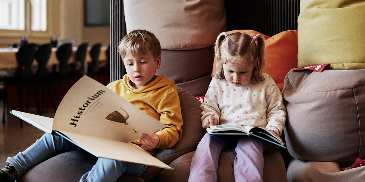 Gutt og jente sitter på puter og leser bøker