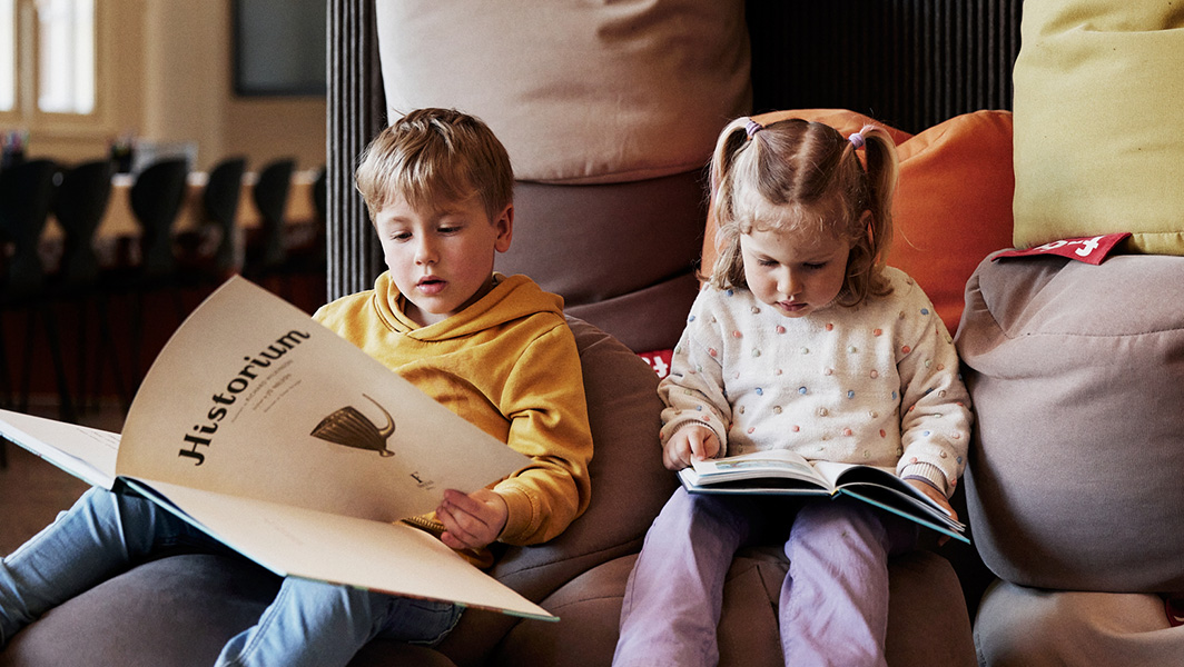 To barn sitter på puter og leser bøker