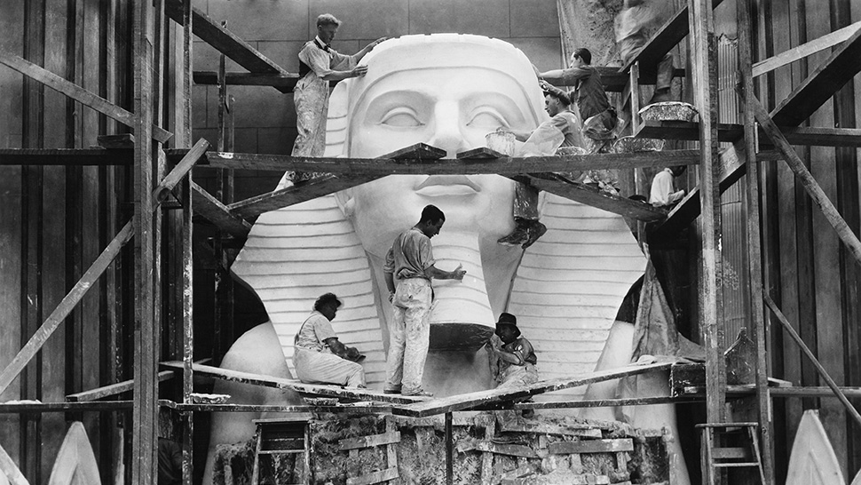 Foto av arbeidere på stilas rundt en flere meter høy skulptur av en farao 