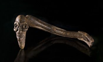 Rått bearbeidet trefigur fra Påskeøya (Rapnui)&amp;#160;i Polynesia. Slike figurer kalles&amp;#160;Moai kavakava&amp;#160;og fremstiller et utmagret vesen, halvt menneske halvt dyr. Opprinnelig har figuren hatt innsatte øyne og en snor tredd gjennom hullene langs ryggraden slik at den kunne bæres som hals- brystsmykke i rituelle sammenhenger. Innsamlet av skipsfører Peter Arup under hans opphold på Påskeøya i 1869 og skjenket til Etnografisk museum i 1871.