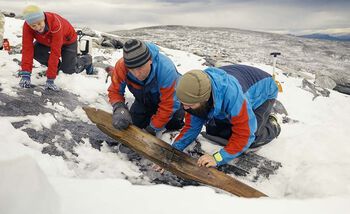 Skien lå begravet med undersiden opp. Her blir den snudd og vi ser oversiden med bindingen. Fra venstre Mai Bakken, fra Norsk fjellsenter, Espen Finstad, fra Secrets of the Ice-prosjektet og Innlandet fylkeskommune, og Julian Post-Melby, fra Kulturhistorisk museum.