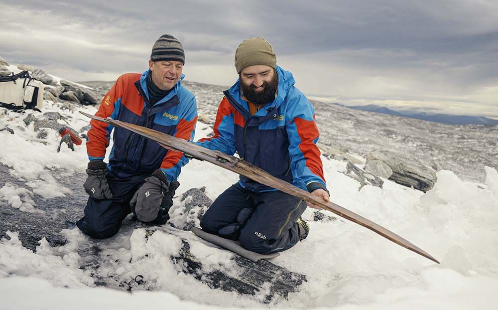 To menn sitter i snøen og holder en treski i hendene.